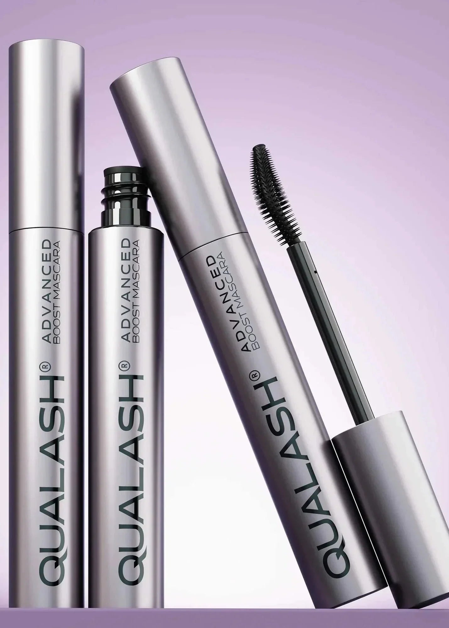 Multiple QUALASH Curl &amp; Lift mascaras arranged creatively on soft purple background with focus on brush and tube