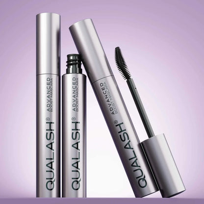 Multiple QUALASH Curl &amp; Lift mascaras arranged creatively on soft purple background with focus on brush and tube